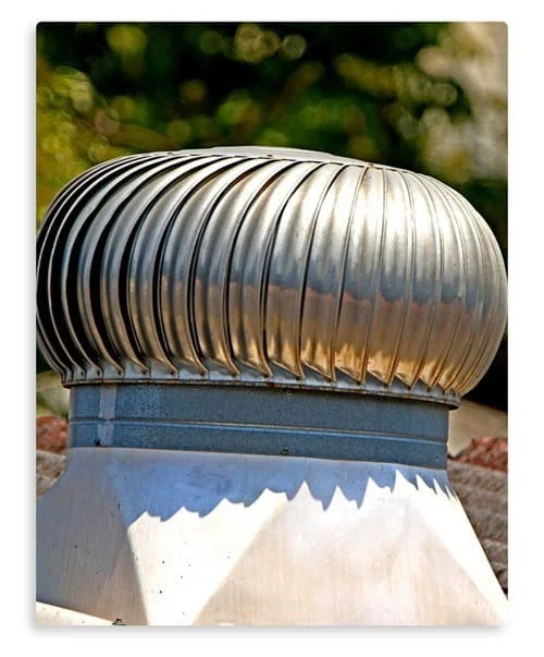 A shiny metal turbine attic fan sits on a white base