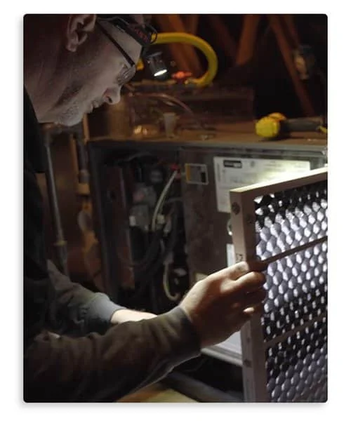 A technician wearing a headlamp carefully removes an air filter from an HVAC unit