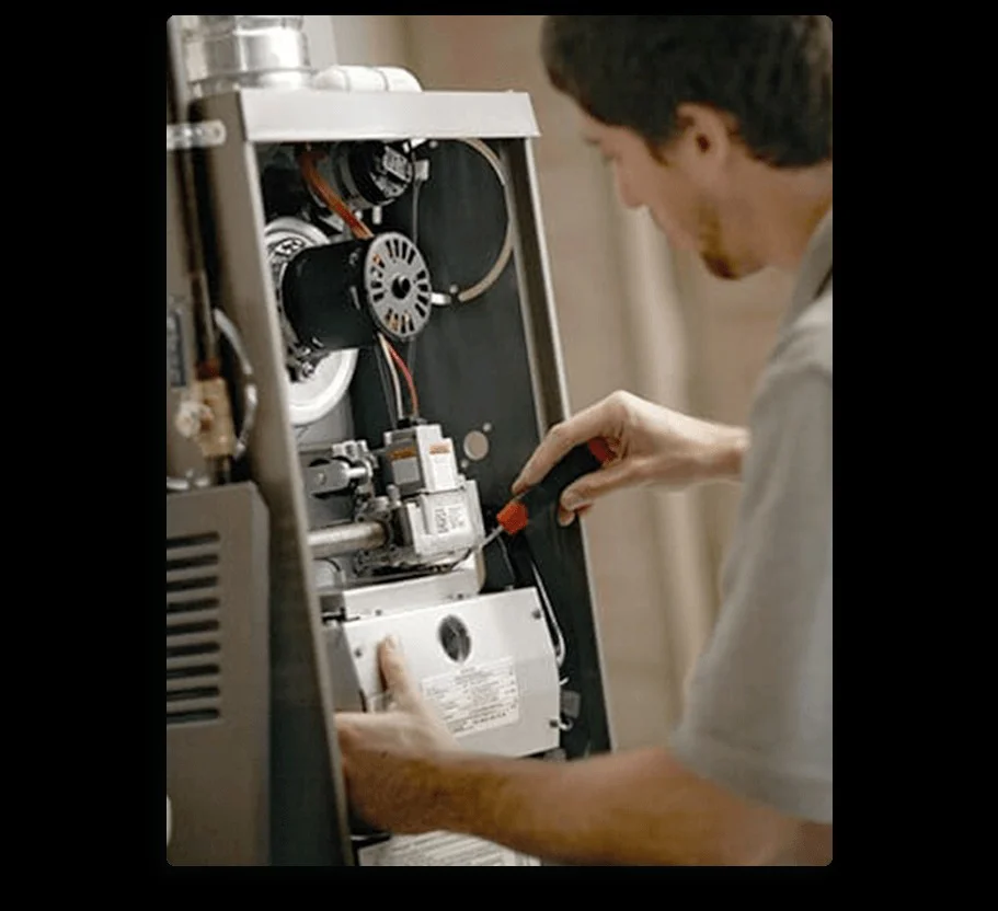 A technician uses a screwdriver to service the internal components of a furnace or HVAC unit