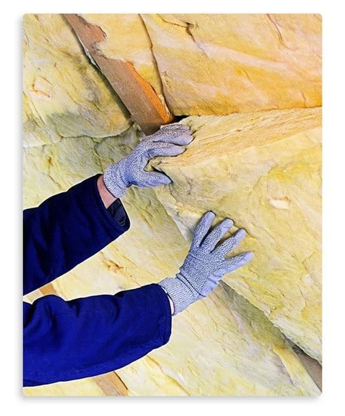 A pair of gloved hands installs yellow insulation material